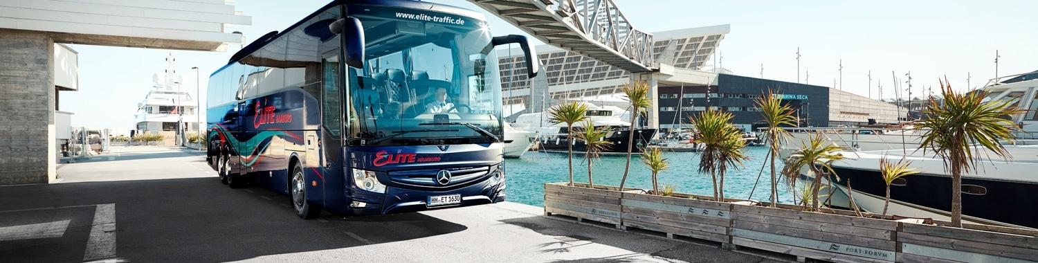 Ein moderner Elite Reisebus für 59 Personen fährt entlang eines Sportboothafens